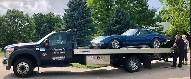 The black Ultimate Towing flatbed carrying a blue Corvette